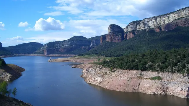 El pantano de Sau con los acantilados de Tavertet al fondo y el campanario de la iglesia sumergida asomando sobre el agua.