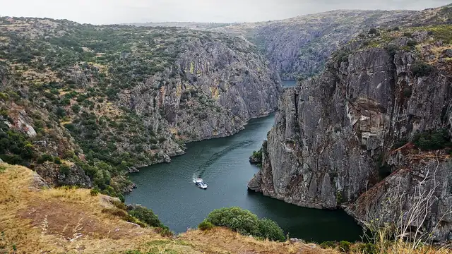 El río Duero encajado entre los acantilados de granito del parque natural de Arribes, con un catamarán navegando aguas abajo.